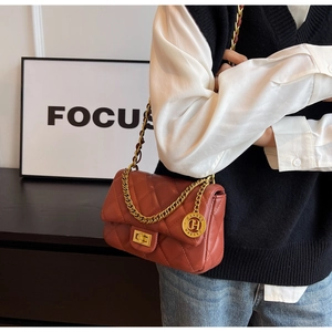 Detail of brick red quilted leather crossbody bag with golden chain and clasp closure