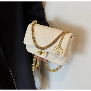 Close-up of beige quilted crossbody bag with gold chain and circular metal charm detail