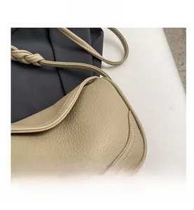 Detail of beige lychee textured leather crescent bag with woven shoulder strap