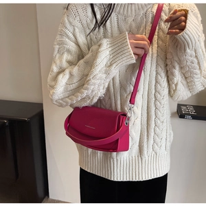 Détail du sac bandoulière rose fuchsia en cuir grainé sur un pull en maille blanche