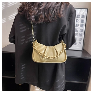 Detail of ruched yellow faux leather handbag with gold chain strap worn by a model