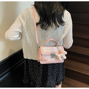 Detail of pink designer handbag with silver lock and plush dog charm worn by a model