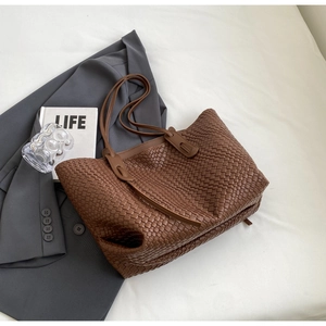 Detailed view of large brown woven tote bag on bed with urban lifestyle accessories