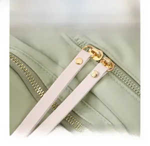 Macro shot of smooth gold metal zippers with pink leather pulls on a green nylon backpack