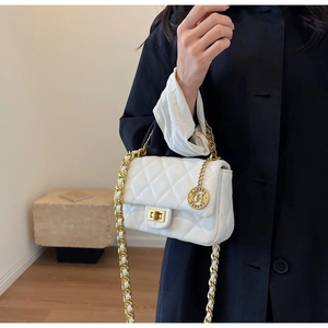 Detail of white quilted crossbody bag with gold chain strap and circular metal charm