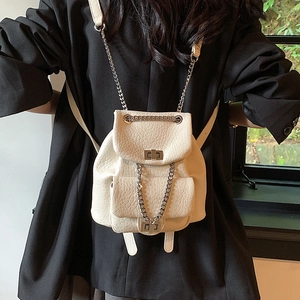 Cream mini bucket backpack with chain straps and faux crocodile texture on black suit
