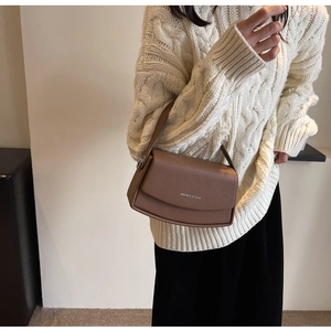 Sac sous le bras marron à motif litchi et logo argenté porté avec un pull blanc