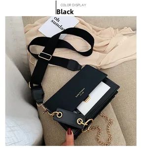 Détail d'un sac bandoulière noir et blanc avec chaîne dorée sur un canapé beige