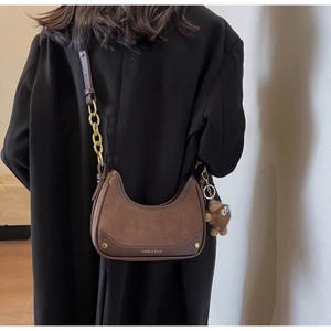 Détail d'un sac croissant marron avec texture en daim et bandoulière en chaîne dorée