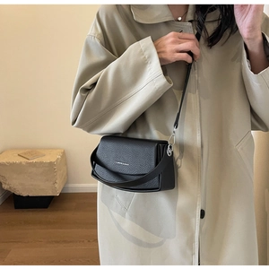 Détail d'un petit sac carré noir en cuir grainé porté avec un trench-coat beige chic