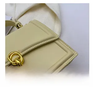 Detail view of smooth beige leather handbag featuring golden metal rings and fine stitching