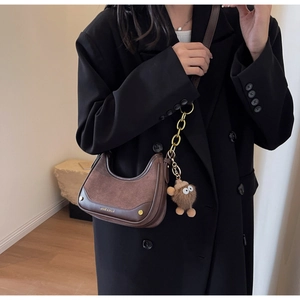 Détail d'un sac demi-lune marron avec pendentif monstre en peluche et chaîne dorée