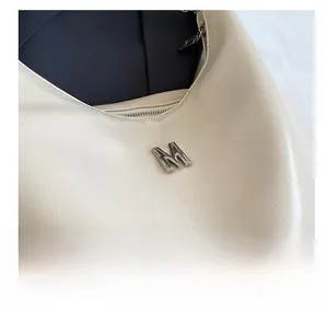 Detail of silver M logo buckle on cream faux leather handbag with lychee grain texture