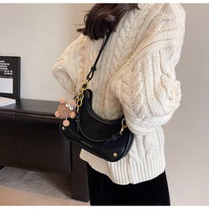 Détail du sac hobo en croissant noir avec chaîne dorée et accessoire en peluche ours brun