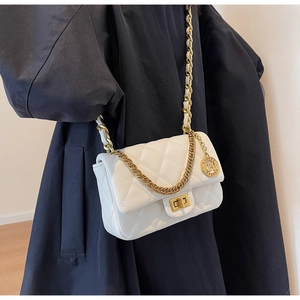 Detail of white quilted crossbody bag with gold chain strap and brand charm on model