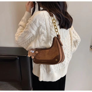 Détail du sac croissant en daim marron avec chaîne dorée et porte-clés en peluche