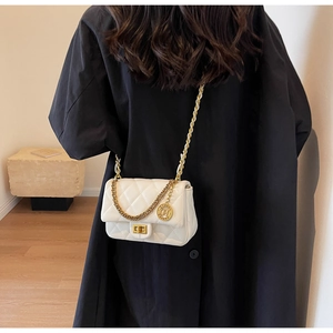 Detail of white quilted crossbody bag with golden chain strap and round metal pendant