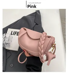 Pink lychee texture leather saddle bag featuring a woven handle and elephant charm