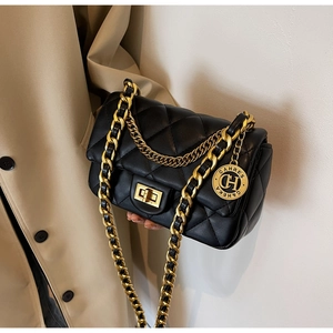 Detailed close-up of a black quilted leather bag with gold chain and brand charm tag