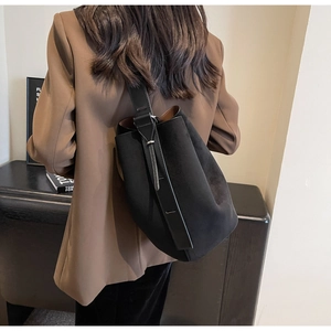 Détail du sac seau en daim noir avec bandoulière en cuir porté sur un blazer marron