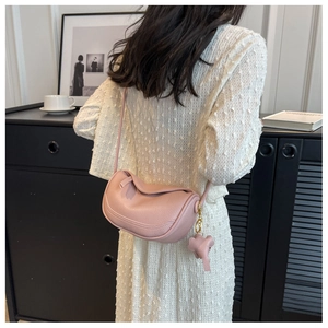Detail of pink pebbled leather dumpling crossbody bag with cute elephant charm on a model