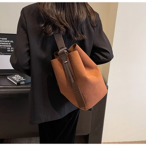 Détail du sac seau mat caramel avec large bandoulière réglable porté sur un blazer noir