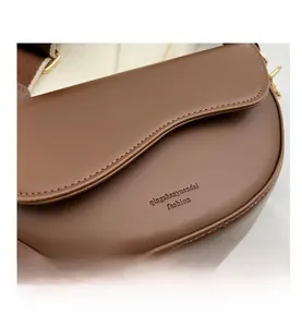 Close-up of brown leather saddle bag featuring textured grain and wide fabric strap