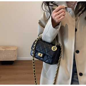 Close-up of black quilted shoulder bag with golden chain strap and round brand pendant