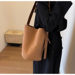 Détail d'un sac seau en daim marron avec bandoulière large et finitions métalliques fines