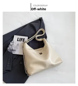 Detail of cream hobo bag with adjustable strap and decorative metal chain on grey blazer