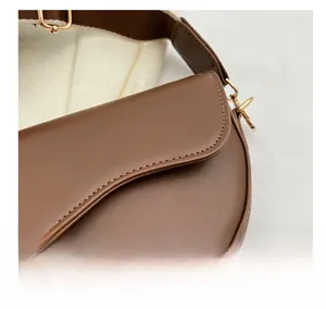 Close-up of dark brown saddle bag with precise stitching and gold hardware detail