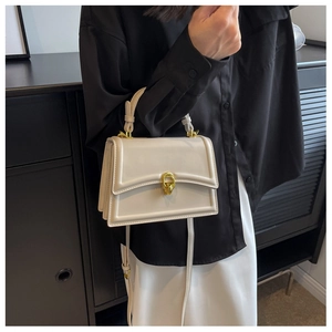 Close-up of cream-white leather handbag with gold chain buckle and adjustable strap