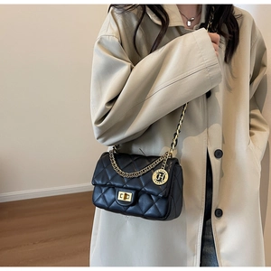 Detail of black quilted shoulder bag with gold chain strap on beige trench coat