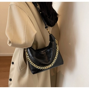 Détail du sac à bandoulière en cuir plissé noir avec chaîne dorée sur manteau beige