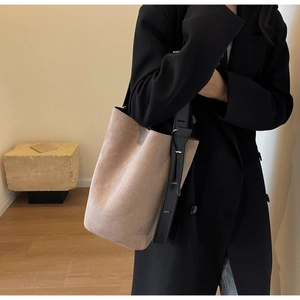 Détail d'un sac seau en daim givré avoine avec une large bandoulière noire stylée