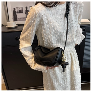 Detail of black crossbody dumpling bag with woven strap and elephant charm on white dress