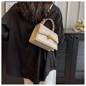 Modern creamy white crossbody bag with golden ring clasp shown on a model