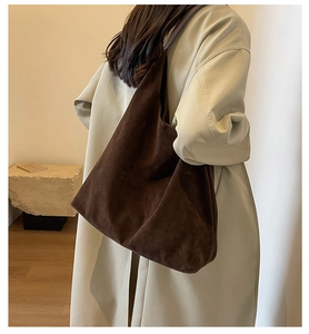 Close-up of a large brown matte suede tote bag worn by a model in a minimalist setting