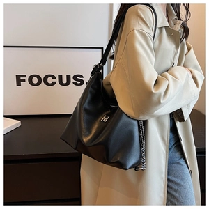 Close-up of black lychee leather shoulder bag with metal M logo and chain strap detail