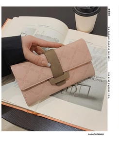 Portefeuille rose en cuir gaufré de trèfles avec boucle élégante tenu par une femme