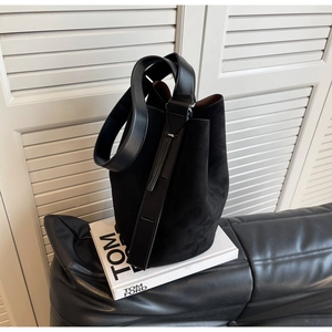 Détail d'un sac seau en daim noir avec bandoulière en cuir sur fond de livre de mode