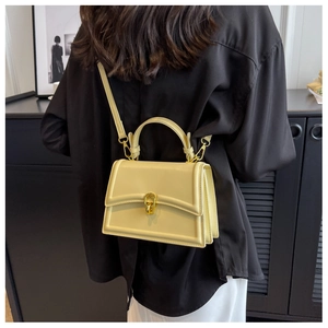 Rear view of model wearing beige crossbody bag with gold chain lock and handle detail