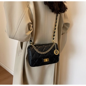 Detailed view of black quilted crossbody bag with gold chain strap on model in beige coat
