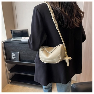 Detail view of beige crescent bag with woven strap and elephant charm on model