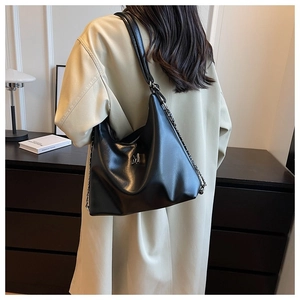 Detail of black faux leather hobo bag with silver metal M logo and chain strap