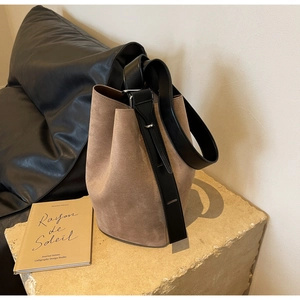 Détail du sac seau mat beige avec bandoulière en cuir noir sur une surface en pierre