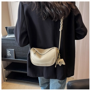 Detail of off-white lychee grain leather saddle bag with woven strap and elephant charm