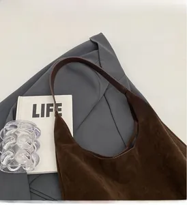 Detail of dark brown suede Hobo bag featuring wide leather strap on a grey blazer