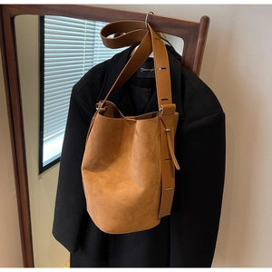 Gros plan sur un sac seau en daim marron mat avec large bandoulière sur un manteau noir