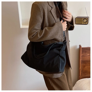 Close-up of a large black minimalist hobo bag worn over a brown herringbone blazer jacket